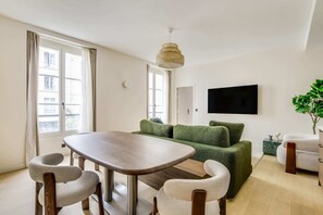 A modern living room with a dining table, green sofa, and a flat-screen TV mounted on the wall. - Gorgeous Air-conditioned 2-BR/2Ba  - Saint-Germain (Paris)