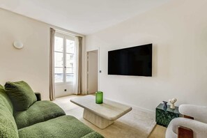 A living room with a sofa, a coffee table, a TV mounted on the wall, and a door leading to an outdoor area. - Gorgeous Air-conditioned 2-BR/2Ba  - Saint-Germain (Paris)