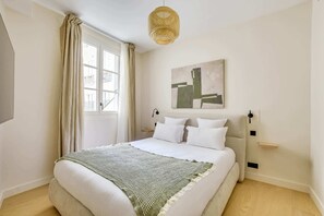 A modern bedroom with a large bed, a window with curtains, a wall-mounted artwork, and a hanging light fixture. - Gorgeous Air-conditioned 2-BR/2Ba  - Saint-Germain (Paris)