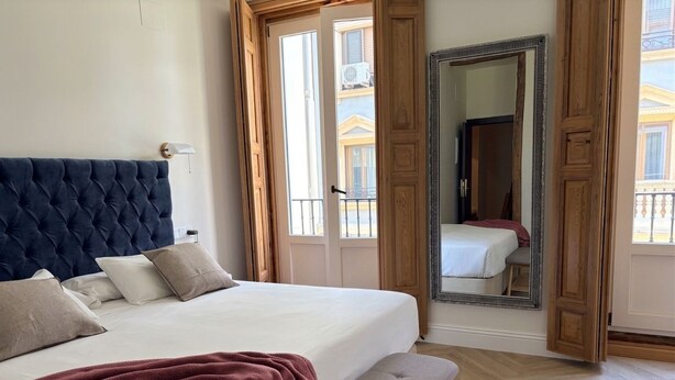Un dormitorio con una cama grande, un banco, un espejo y vistas al exterior.