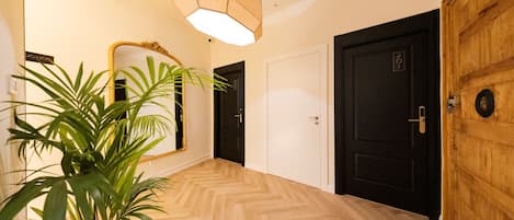 En gang med trægulv, et stort spejl, en potteplante og en dør med nummerplade.