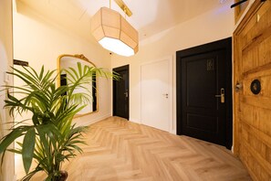 A hallway with a wooden floor, a large mirror, a potted plant, and a door with a number plate. - Alistana Boutique Gran Vía   (Madrid)
