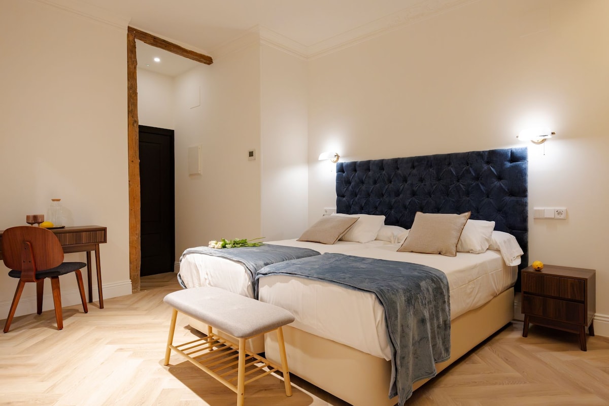 Un dormitorio con una cama grande, mesitas de noche, un banco y un escritorio con una silla.