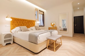Un dormitorio con una cama grande, mesitas de noche, un banco, un espejo y una puerta.