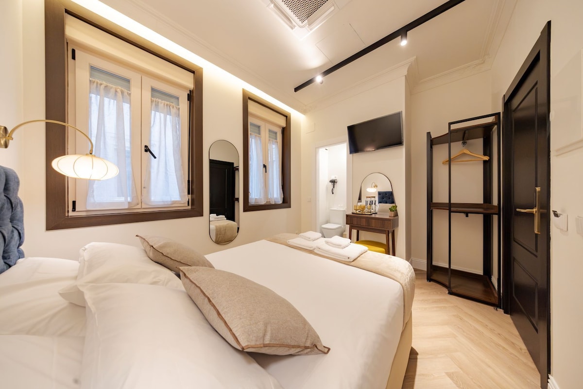 Una habitación de hotel con cama, mesitas de noche, un espejo, televisor y armario.