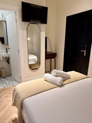 Una habitación de hotel con una cama, un espejo, un televisor, una puerta y una mesita.