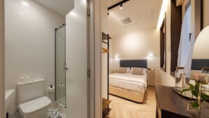 Una camera d'albergo moderna con doccia, wc, letto, comodino e specchio.