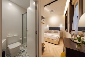 Habitación de hotel moderna con ducha, inodoro, cama, mesita de noche y espejo.