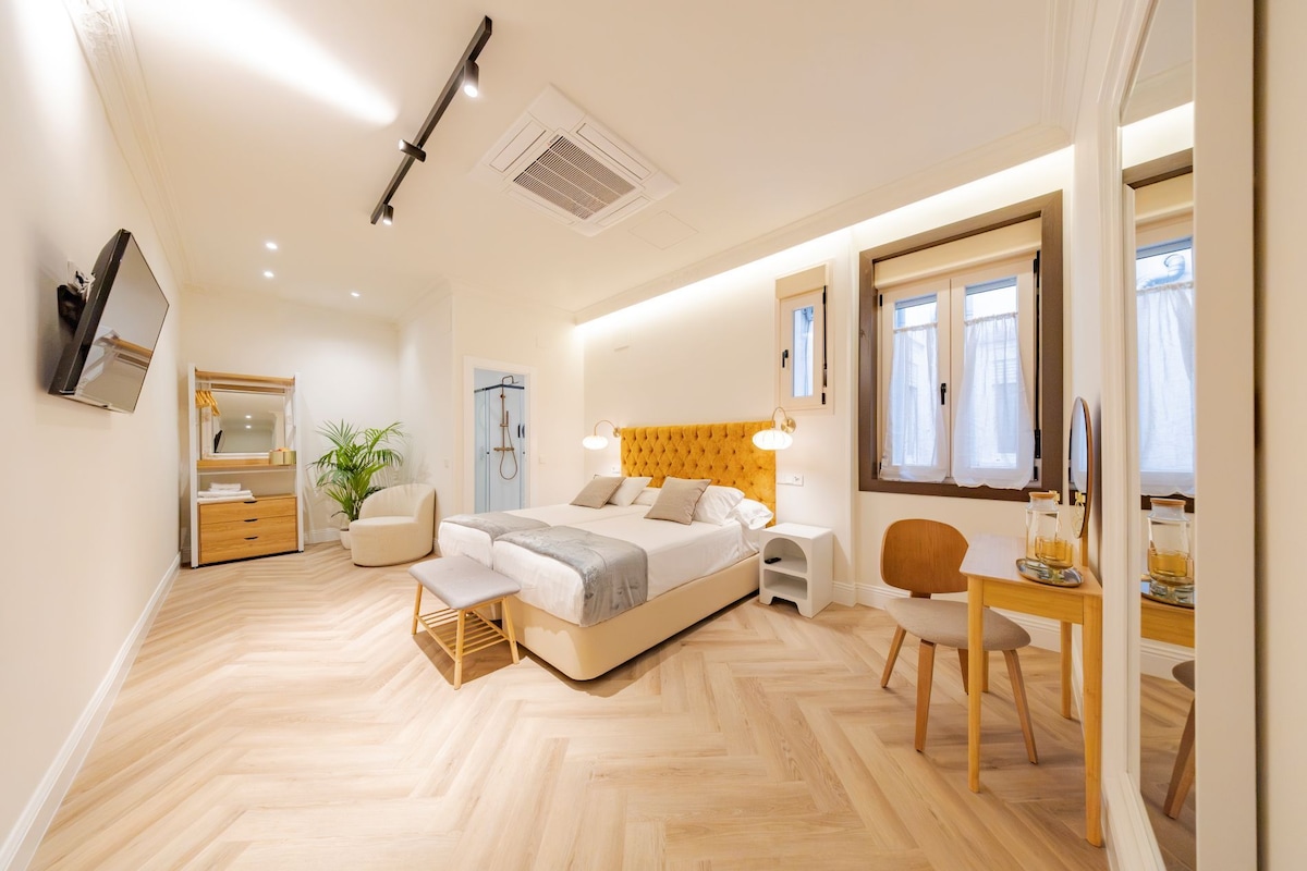 Un dormitorio moderno con cama, mesita de noche, sillón y escritorio con silla.