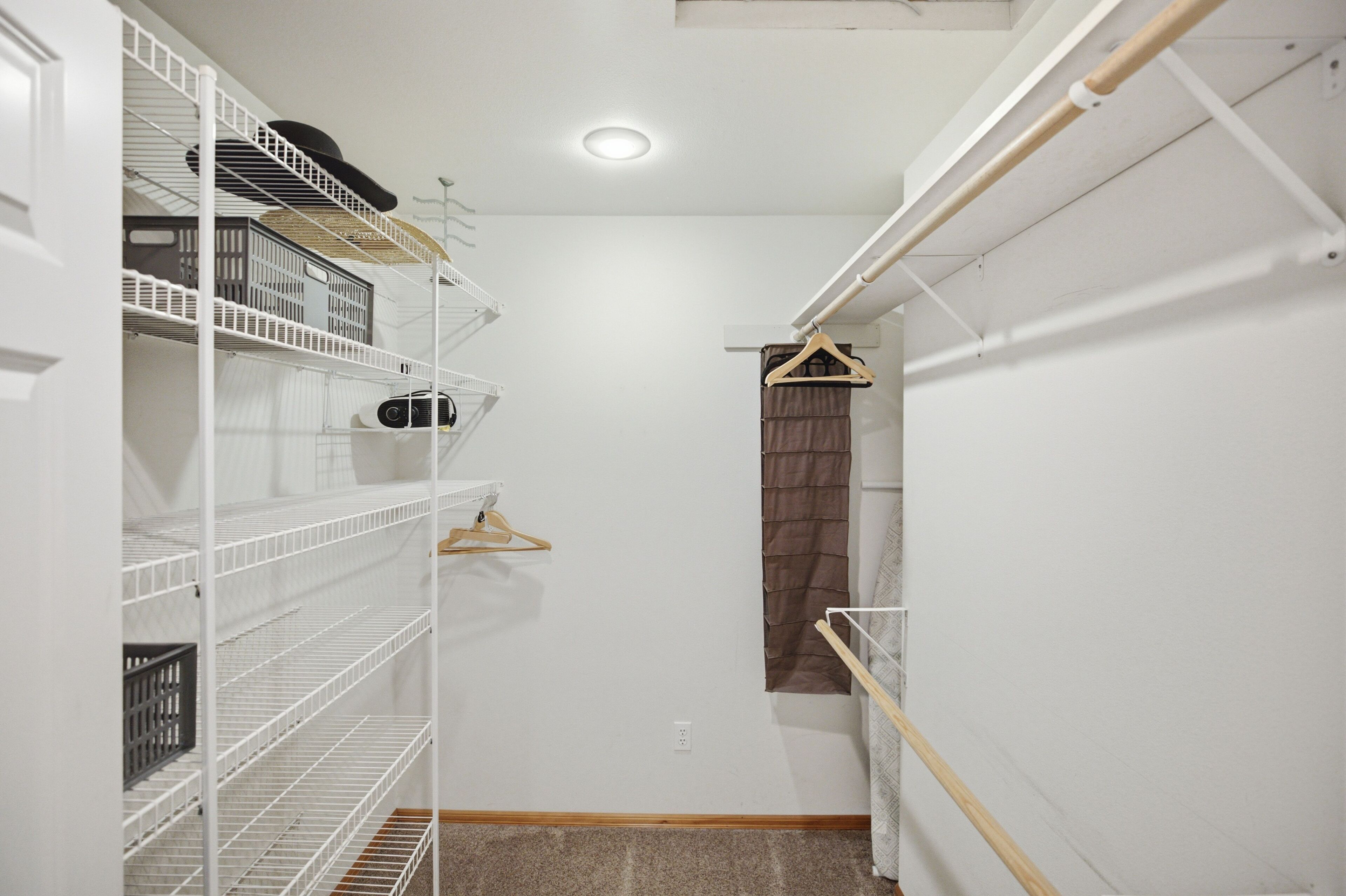 Ein begehbarer Kleiderschrank mit weißen Regalen, einer Kleiderstange und einem kleinen Fenster mit Vorhang.