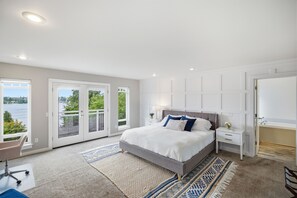 Ein Schlafzimmer mit Bett, Schreibtisch und Blick auf ein Gewässer durch die Fenster.