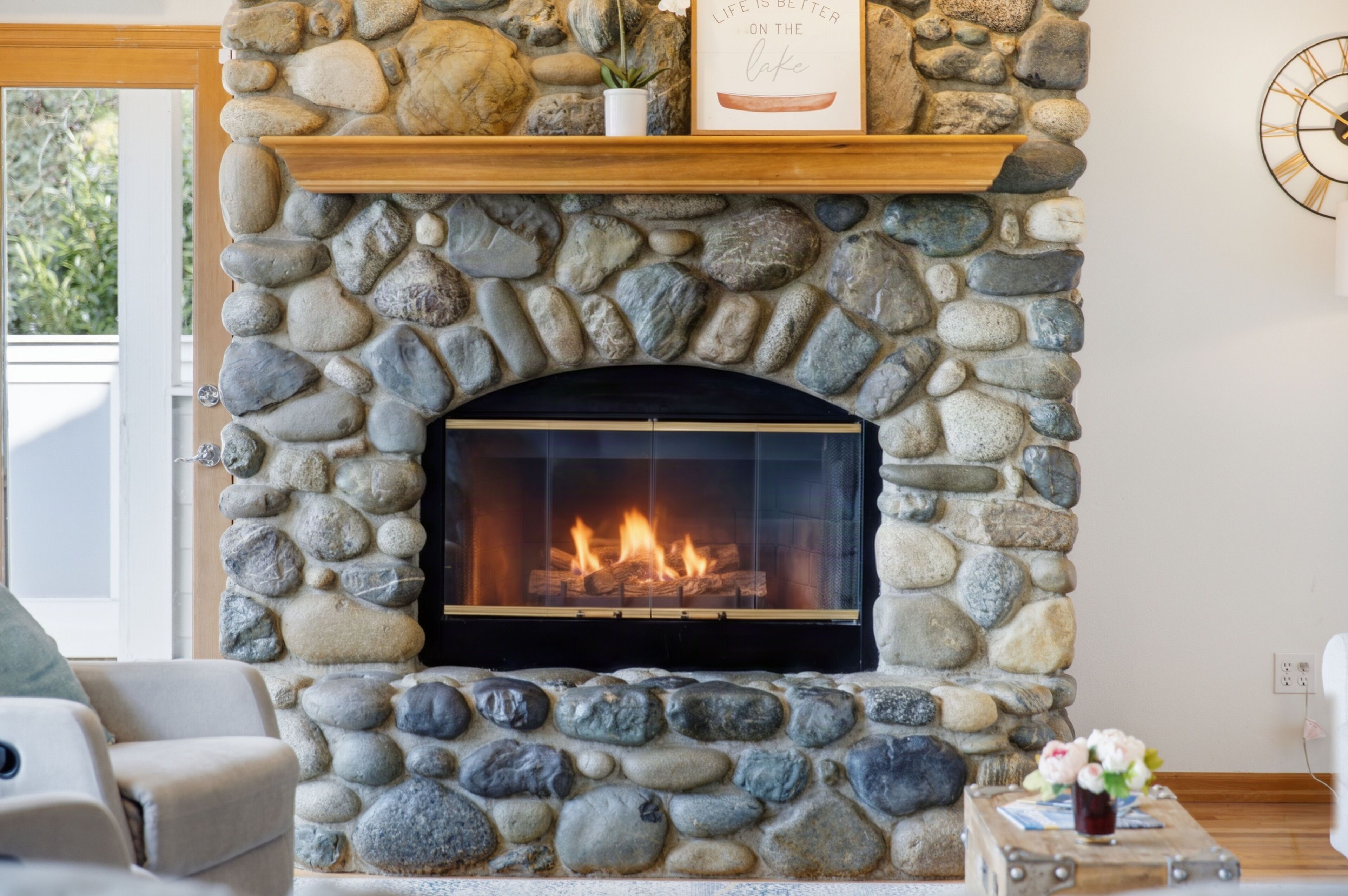 A stone fireplace with a fire, a wooden shelf above it, and a framed quote on the wall.