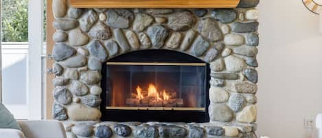 A stone fireplace with a fire, a wooden shelf above it, and a framed quote on the wall.