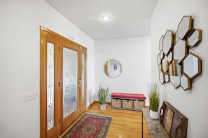 Ein Flur mit Holzboden, einer roten Bank, einem Wandspiegel und einer geometrischen Wanddekoration.