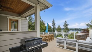 Eine Terrasse im Freien mit Grill, Holzmöbeln und Blick auf einen See.