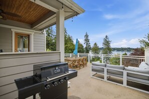 Eine Terrasse im Freien mit Grill, Holzmöbeln und Blick auf einen See.