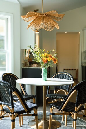 A dining area with a round table, four chairs, a vase with flowers, and a hanging light fixture. - Livin' La Vida Lakehouse (Henrico)