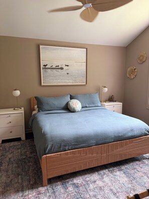 Ein Schlafzimmer mit Bett, Nachttischen, Deckenventilator, Wandbild und dekorativer Wandgestaltung.