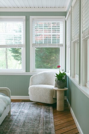 Een kamer met een raam, een stoel, een klein tafeltje met een plant en een kamerbreed tapijt.