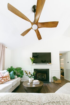 Un salon équipé d’un ventilateur de plafond, d’une cheminée, d’un téléviseur et d’un canapé.