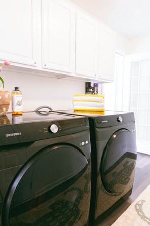 Een wasruimte met twee Samsung wasmachines, een gele handdoek en een fles wasmiddel.