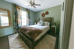 Une chambre à coucher avec un lit, un ventilateur de plafond, une fenêtre avec des rideaux et une horloge fixée au mur.