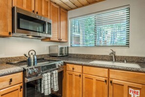 A kitchen with wooden cabinets, a stainless steel microwave, a toaster, a kettle, a stove, and a window with blinds. - Beautiful updated Courchevel by the Slopes. Sleeps up to 8 guests! (Mammoth Lakes)