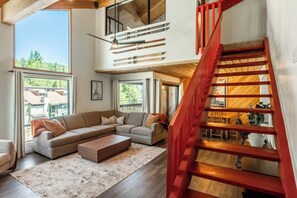 A spacious living area with a large sectional sofa, a wooden coffee table, and a red staircase. - Beautiful updated Courchevel by the Slopes. Sleeps up to 8 guests! (Mammoth Lakes)