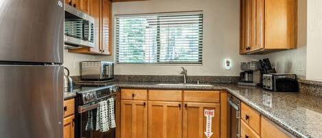 A kitchen with wooden cabinets, stainless steel appliances, a window with blinds, and a fire extinguisher sign.