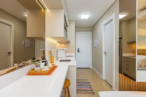 A modern hotel room with a kitchenette, a large mirror, a bed, and a view of the hallway. - Modern Studio with a View in Downtown Curitiba - Luxury (Curitiba)