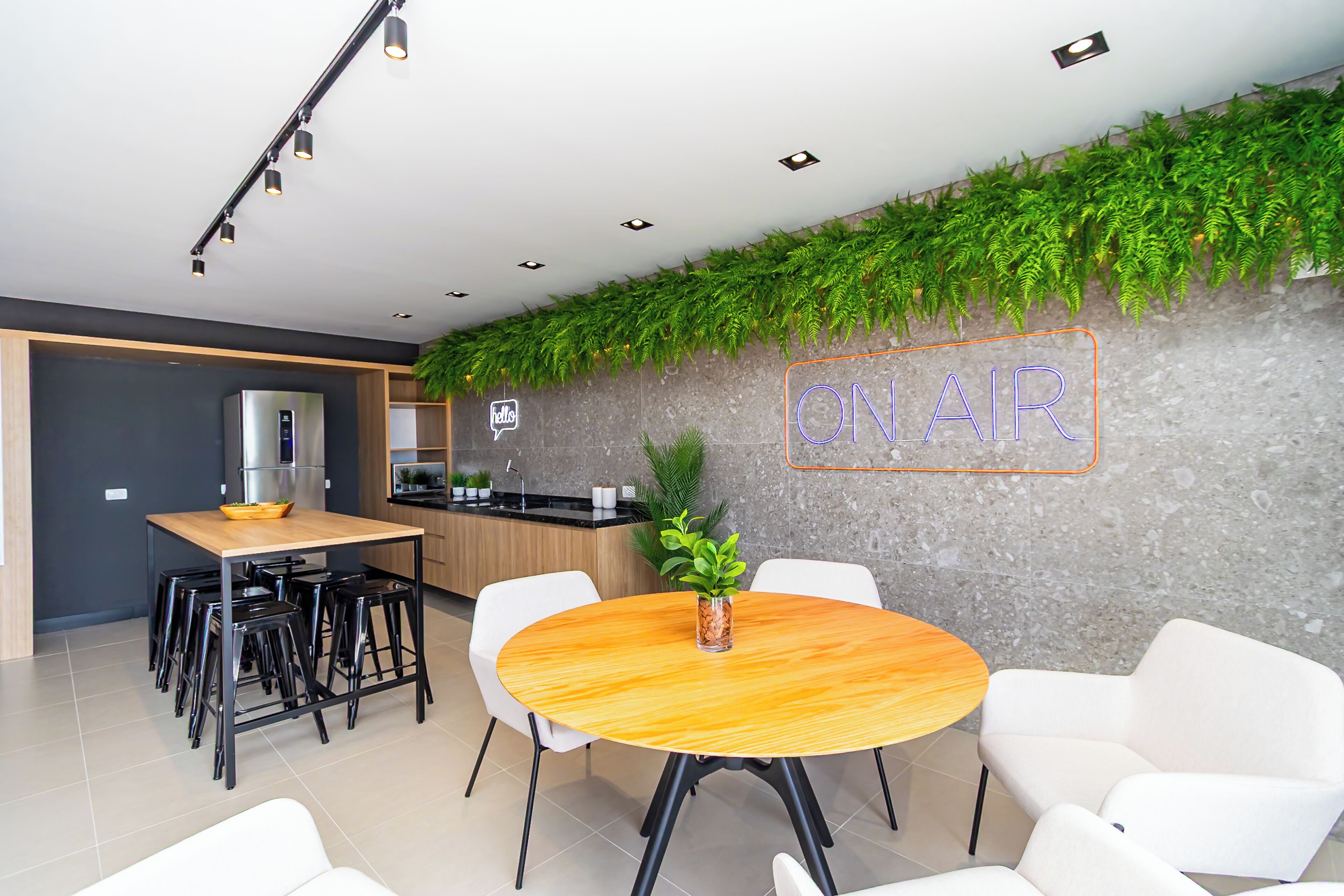 A modern kitchen with a built-in refrigerator, a wooden dining table with chairs, and a neon sign that reads 'ON AIR' on the wall.