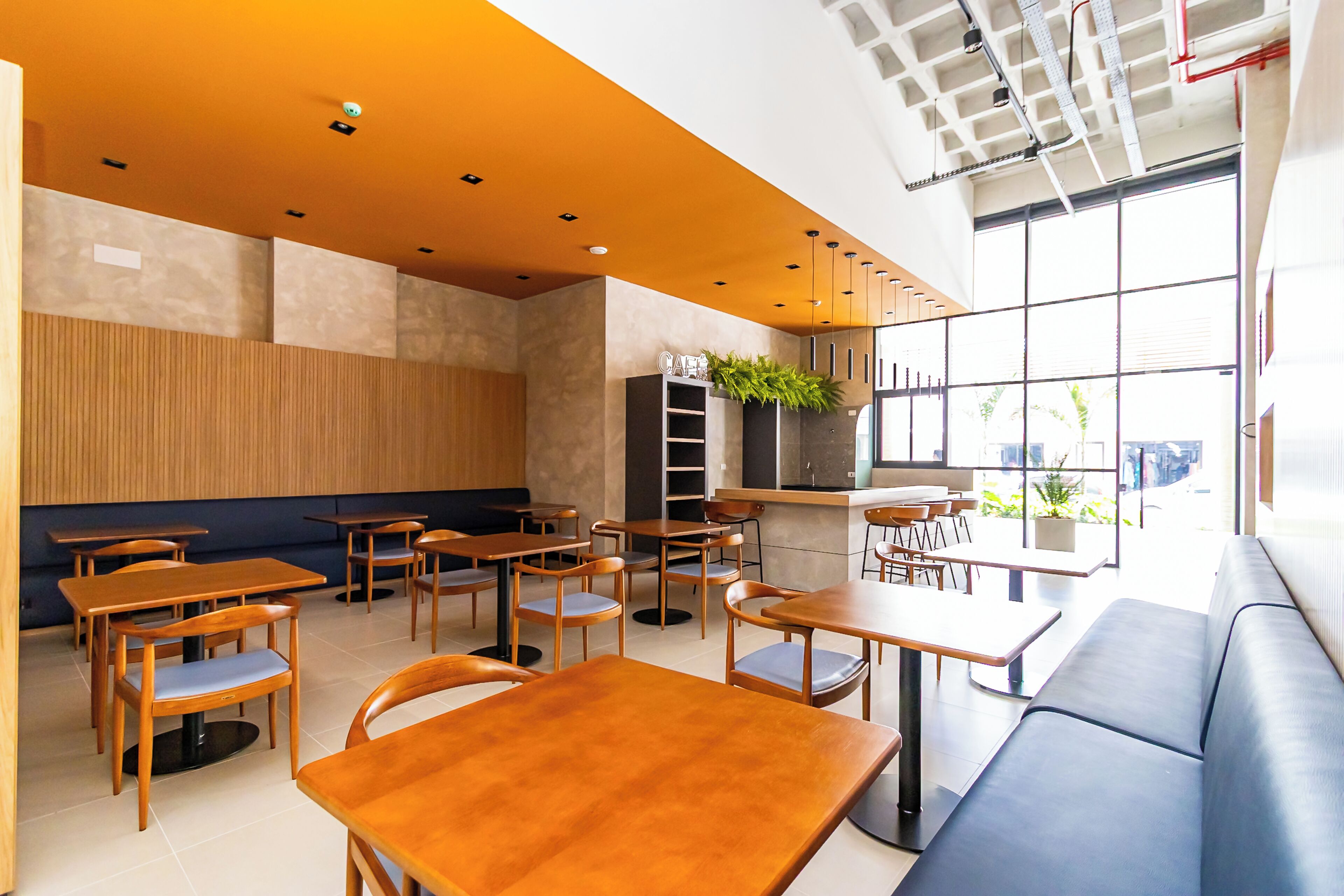 L'intérieur d'un café moderne, avec des tables et des chaises en bois, un comptoir et une grande fenêtre donnant sur l'extérieur.