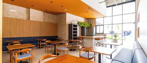 Un interior de cafetería moderno con mesas y sillas de madera, una barra y un ventanal que ofrece vistas al exterior.