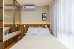 A hotel room with a bed, a bedside table, a mirror, an air conditioning unit, and two framed pictures on the wall. - Modern Studio with a View in Downtown Curitiba - Luxury (Curitiba)