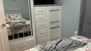 A bedroom with a bed, a dresser with drawers, a television on top, and a door leading to another room. - Cozy 1-bedroom tiny home in resort setting (Citra)
