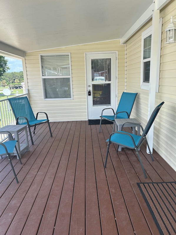 A covered porch with a wooden deck, a white door, and two blue chairs. - Cozy 1-bedroom tiny home in resort setting (Citra)