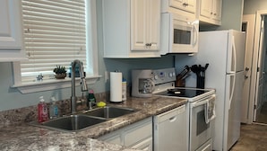 A kitchen with white cabinets, a granite countertop, a stainless steel sink, and a refrigerator. - Cozy 1-bedroom tiny home in resort setting (Citra)