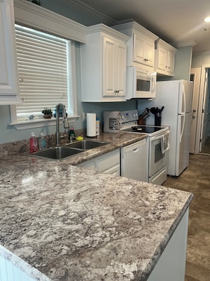 A kitchen with white cabinets, a granite countertop, a stainless steel sink, and a refrigerator.