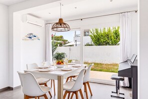 A modern dining area with a white table set for four, surrounded by white chairs with wooden legs. - VILLA MAGDALENA in Cala Blanca (Cala Blanca)