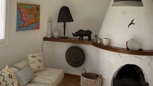 Ein gemütliches Wohnzimmer mit Kamin, einer Couch mit gemusterten Kissen, einem farbenfrohen abstrakten Gemälde und einem Regal mit Dekorationsobjekten.
