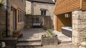A courtyard with stone steps, a wooden bench, potted plants, and a hot tub. - Finest Retreats | Serenity (Painswick)