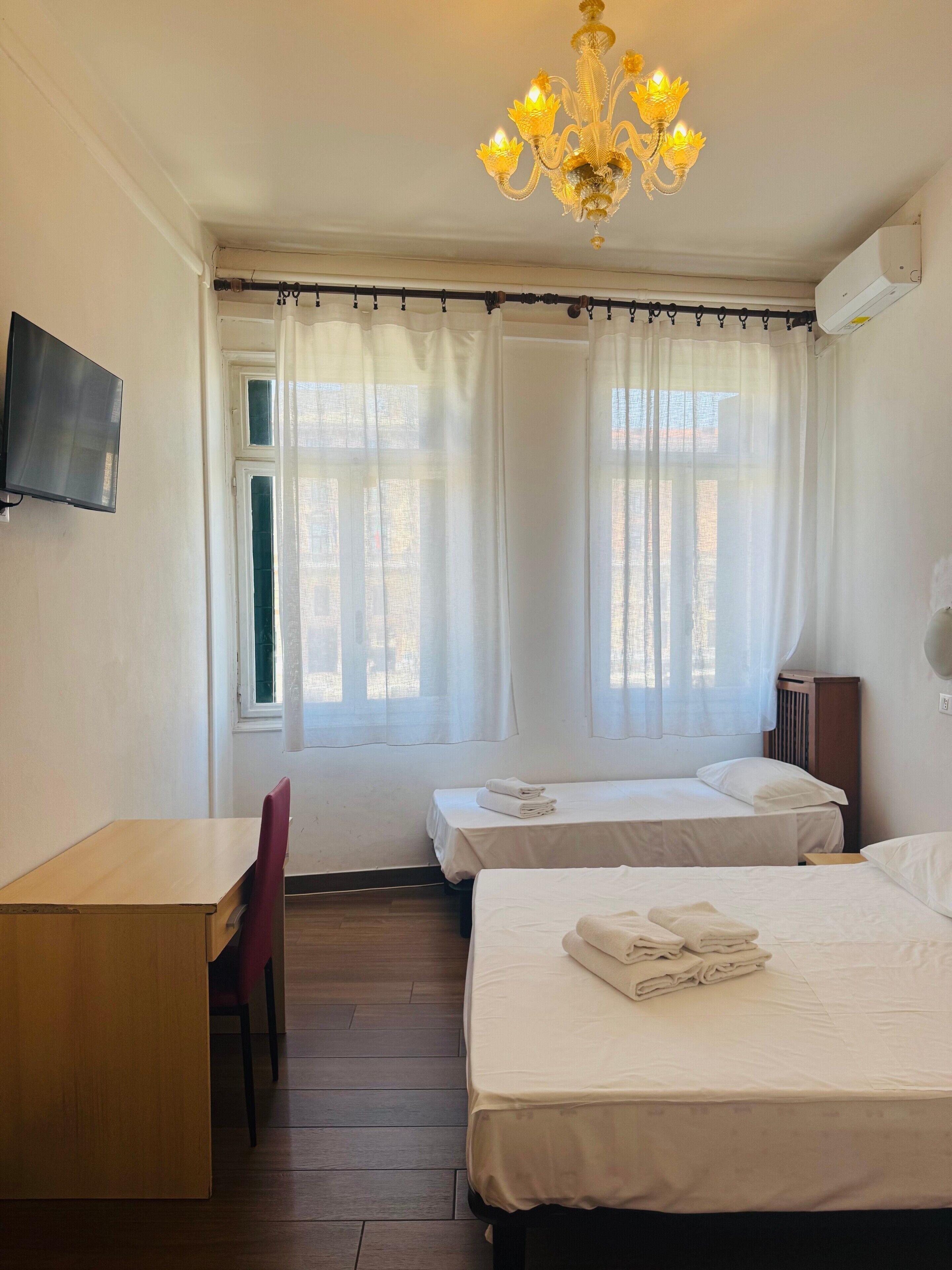 A hotel room with two beds, a desk, a TV, and a chandelier.