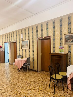 Ein Hotelzimmer mit gemustertem Wandteppich, gefliestem Boden, einem Esstisch mit rosa Tischdecke und einem Stuhl.
