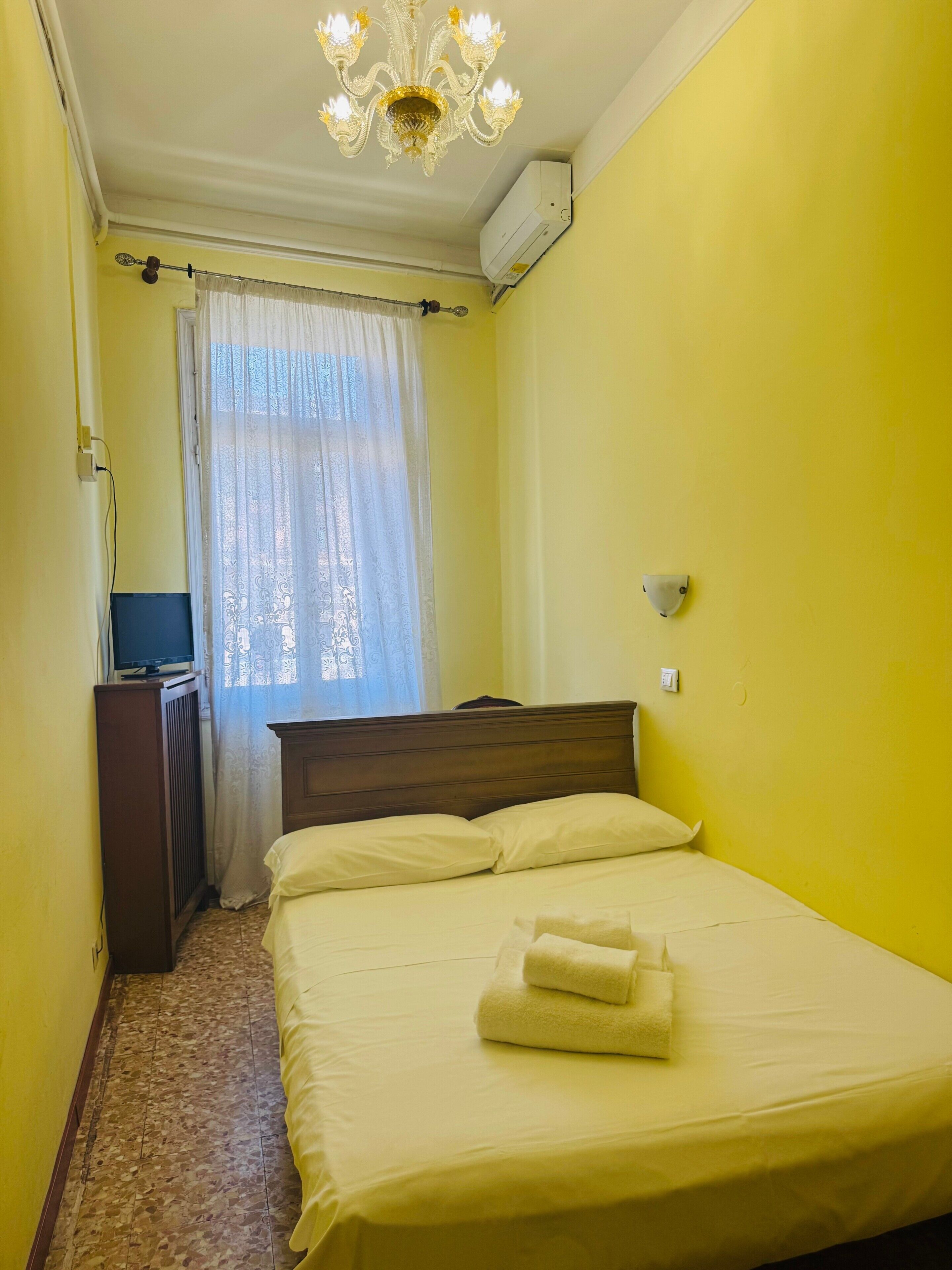 Una habitació amb un llit, un escriptori amb ordinador, una làmpada de cristall i un aparell d'aire condicionat.