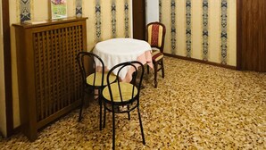 Una stanza con carta da parati decorata, un tavolo rotondo con sedie, un termosifone e una porta.