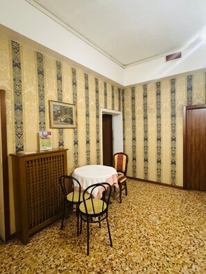 Ein Zimmer mit strukturiertem Wandpapier, einem runden Tisch mit Stühlen, einem Heizkörper und einer Tür.