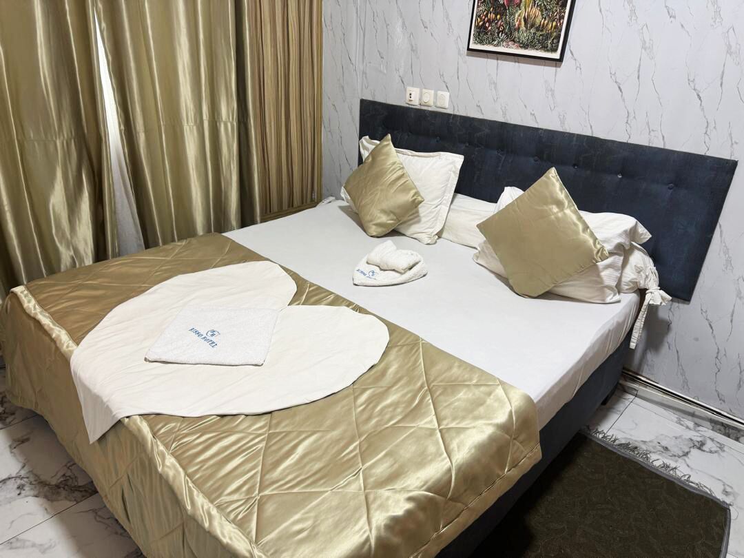 A hotel room with a bed, a headboard, a curtain, a wall-mounted picture, and a marble floor.