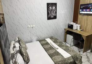 A hotel room with a bed, a desk with a computer, a TV, and a small refrigerator. - BISSO HOTEL (Bonabéri)