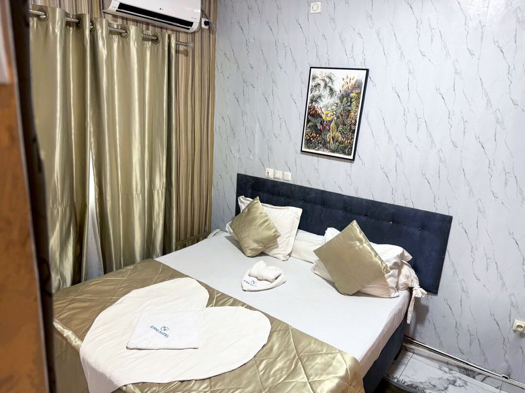 Habitación de hotel con cama, cortinas, equipo de aire acondicionado, un cuadro enmarcado en la pared y un revestimiento de pared con diseño de mármol.
