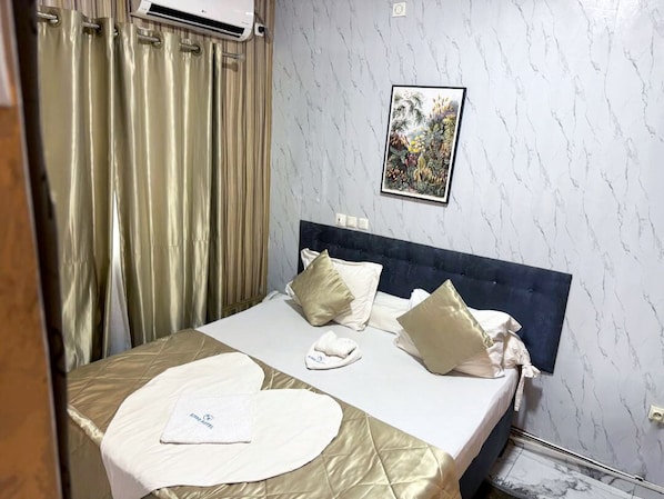 A hotel room with a bed, curtains, an air conditioning unit, a framed picture on the wall, and a marble-patterned wall. - BISSO HOTEL (Bonabéri)
